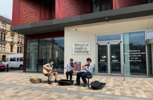 A band with three musicians playing outside the Clarice Pears building