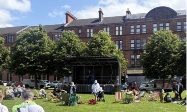 A park with people sitting on deckchairs and a stage with a musician on it