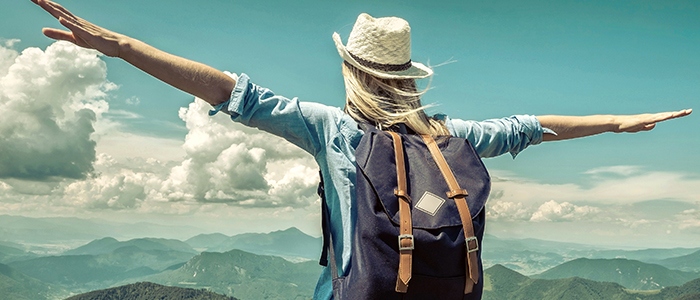 Student standing on a mountain with a backpack on facing a view