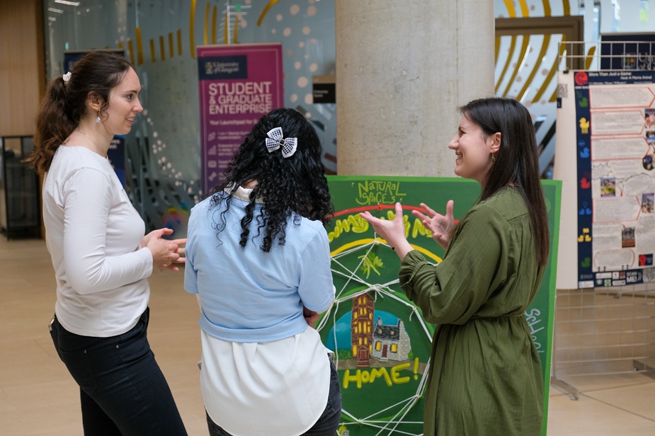 Three females stand beside a green natural spaces display board