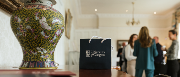 a vase and a university of glasgow branded gift bag on a table. People out of focus in the background are chatting