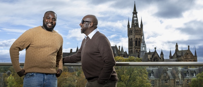 Two men stand on an outdoor platform overlooking Uniersity of Glasgow's main campus.