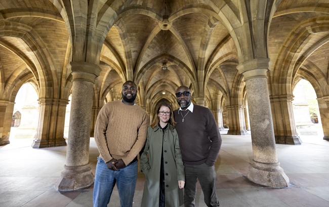 A woman and two men stand in the cloisters of the University of Glasgow.