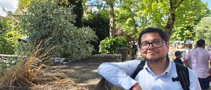 Image of visiting professor from the Indian Institute of Management, standing in from of a park with lots of trees and bushes in the background