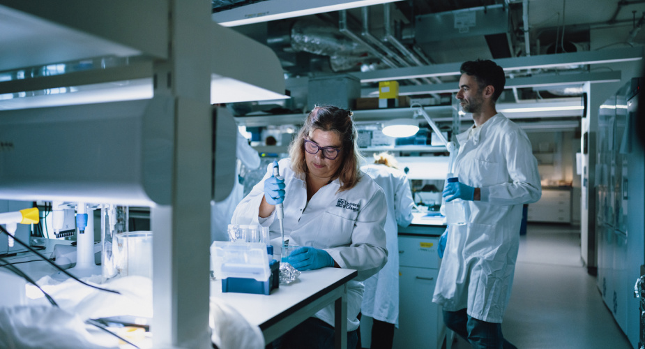 Professor Caroline Gauchotte-Lindsay (centre of photo) with colleagues Prof Caroline Gauchotte-Lindsay wearing a lab coat and holding a pipette and test tube in a lab, while three colleagues are working around her, also wearing lab coats