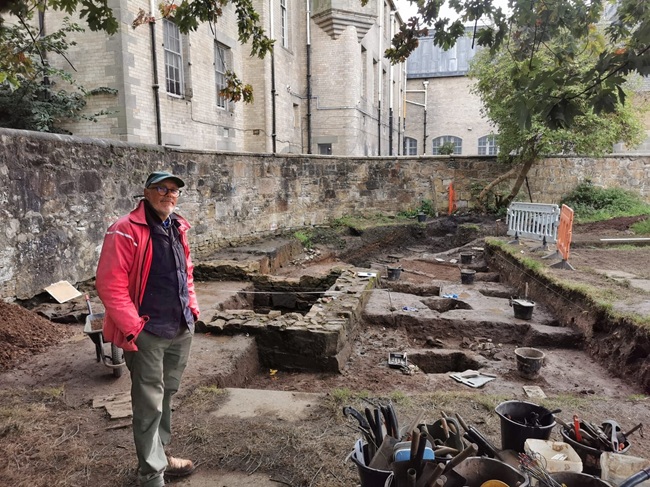 An image of a man standing by an archaeological dig in the ground of an old church yard