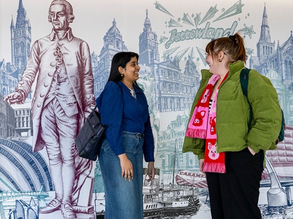 Students standing in front of a wall mural in the Adam Smith Building, Adam Smith Business School