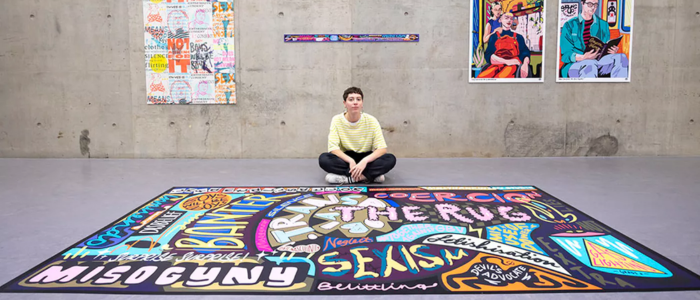 Artist Molly Hankinson sitting cross legged on the floor in the JMSLH surrounded by her artworks for the Together Against Gender Based Violence Campaign