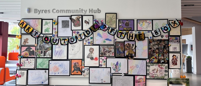 A wall collage of art with the sign 'Art outside the box'