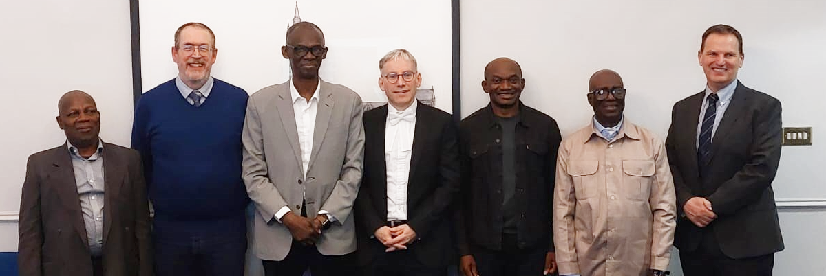 Delegates (Professor Adamu Ahmed; Professor YKE Ibrahim; Professor Iliya S. Ndams, Professor Emmanuel Balogun, Harry de Koning; Andy Schofield, Iain McInnes) stood together in a room in front of a white board and behind a conference table.