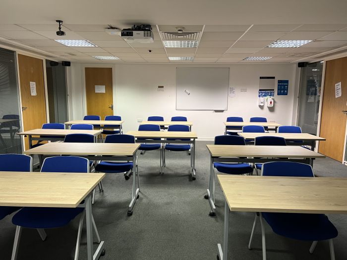 Flat floored teaching room with rows of tables and chairs, whiteboard, and projector.