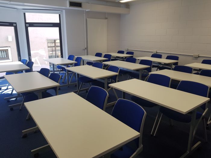 Flat floored teaching room with rows of tables and chairs.