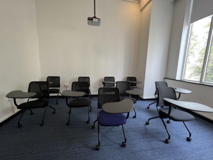 Flat floored teaching room with tablet chairs and projector.