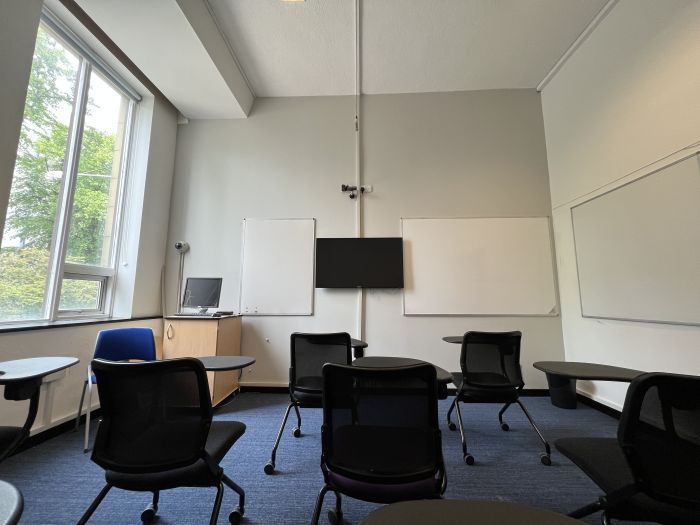 Flat floored teaching room with tablet chairs, whiteboards, video monitor, PC, and lecturer's chair.