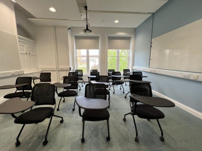 Flat floored teaching room with tablet chairs, whiteboard, and projector.