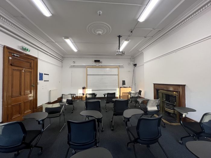 Flat floored teaching room with rows of tablet chairs, whiteboard, projector, lectern, and PC.