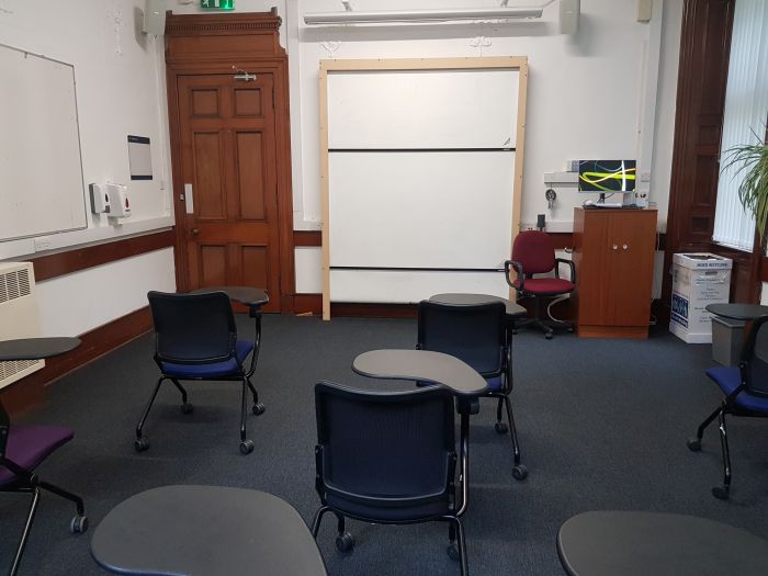 Flat floored teaching room with rows of tablet chairs, whiteboard, and PC
