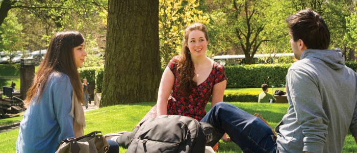 2 female, one male student sitting on grass