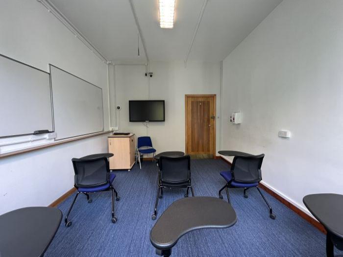 Flat floored teaching room with tablet chairs, whiteboards, video monitor, and lecturer's chair.
