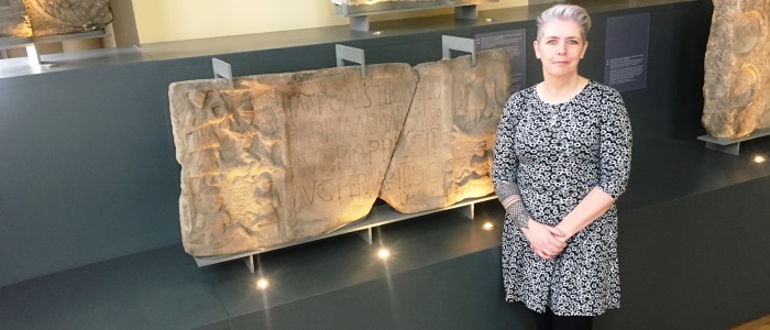 Dr Louisa Campbell in front of Summerston distance stone in The Hunterian 
