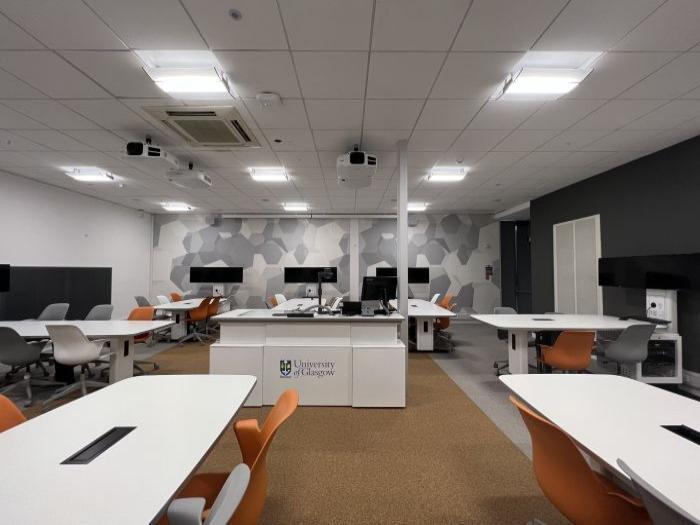 Flat floored Tech Enabled Active Learning (TEAL) room with groups of tables and chairs, each with a video monitor, as well as projectors, visualiser, PC, and lectern.