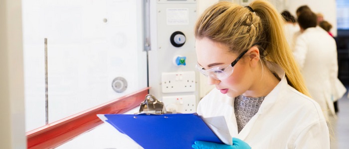 Female researcher doing a health and safety check wearing goggles and clipboard