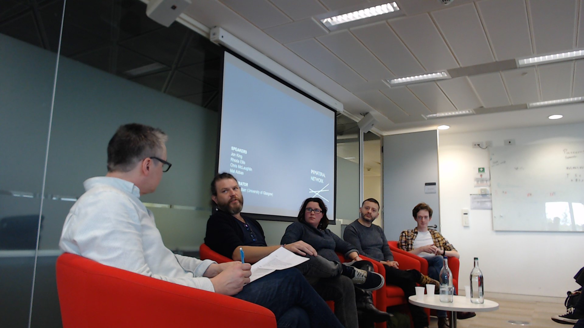 The moderator and four speakers from the third immaterial event, sitting in front of a screen.