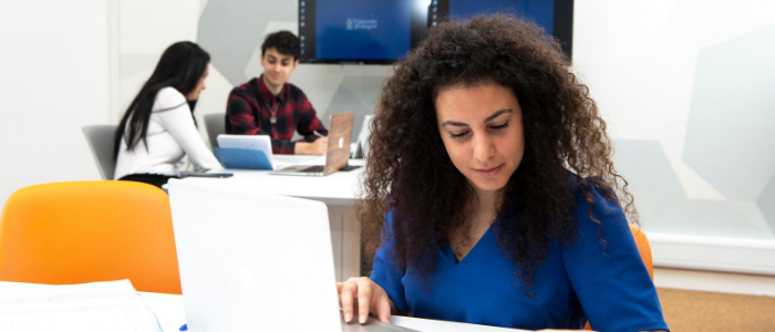 Student studying on a latop in the Hugh Fraser Suite with two students in the background