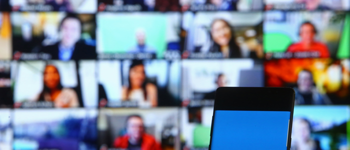 Screen in foreground with wall of screens in background showing people communicating remotely