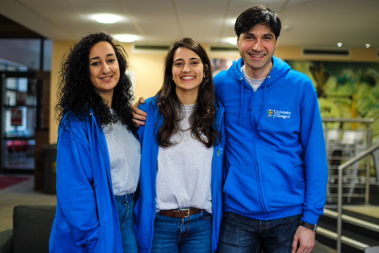 Three Residence Life Assistants wearing blue hoodies and grey t-shirts standing together smiling
