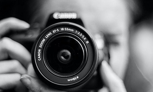 Close up of a camera lens with hands and face of woman holding it out of focus