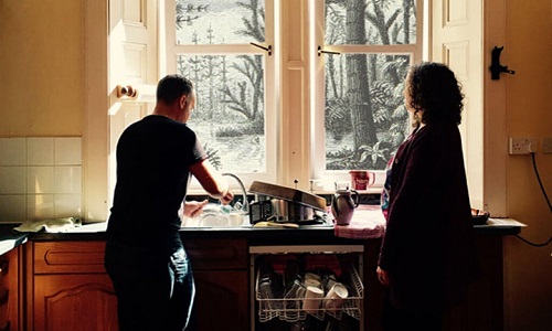 Man washing dishes at sink by window, women standing near by