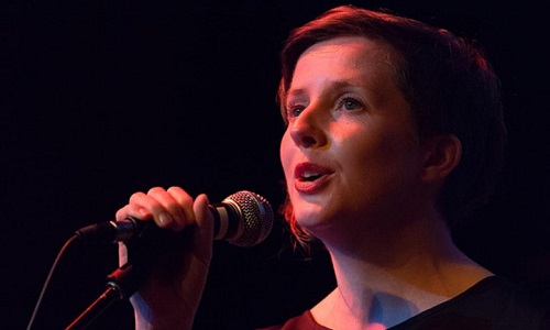 Close up of a woman singing into a mike, dark background and red light on face