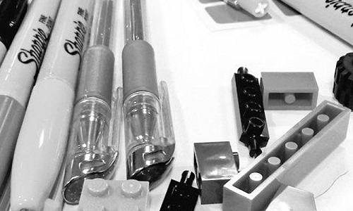 Black and white close up of pens and lego bricks on a white background