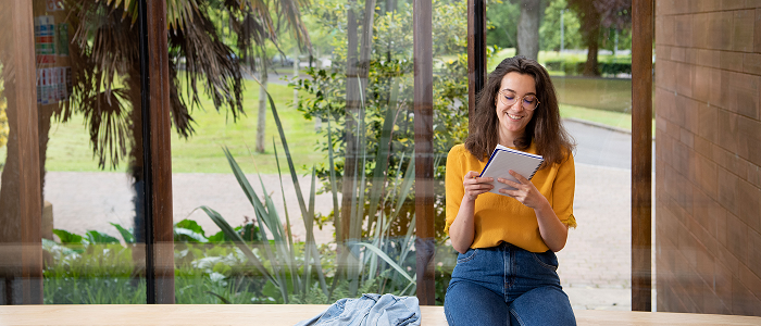Student with book in front of trees - 700x300