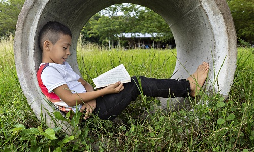 A boy lying inside a concrete pipe in a field and reading a book. Image credit: RECVISUAL | iStockphoto https://www.istockphoto.com/photo/boy-reading-a-book-sitting-on-a-concrete-pipe-on-a-sidewalk-very-happy-and-smiling-gm1295650597-389311729