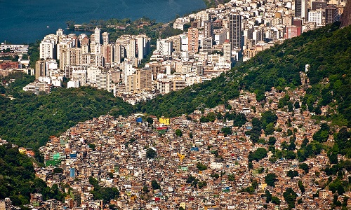 Aerial view of Rio de Janeiro in Brazil with a poorer district called Favela da Rocinha at the forefront and a district with skyscrapers behind, with hilly wooded areas in between. Image credit: dabldy | iStockphoto https://www.istockphoto.com/photo/slum-rocinha-and-aerial-rio-de-janeiro-gm477193287-35532452