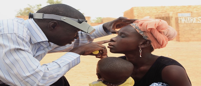 Woman holding baby. She is getting her eye checked by health professional