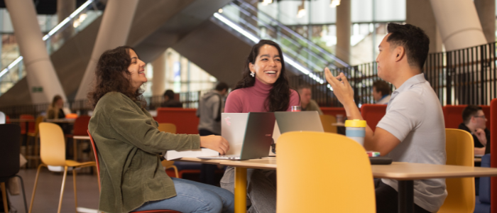 Group of three students sat at a round table laughing and chatting