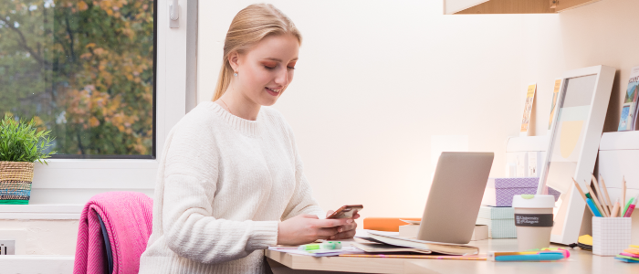 A student saw her desk in front of a laptop but looking at a mobile phone in her hands