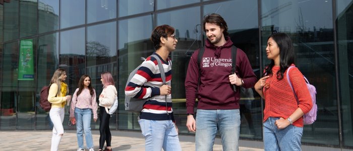 Group of three students with backpacks talking in front of the Fraser building