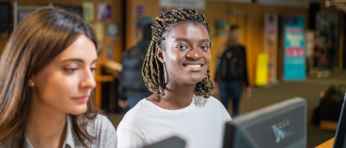 Two young women at standing desks using computers. One is smiling at the camera. Source: Glasgow University Image Library