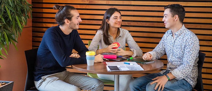 Three people, two men and a woman, chatting at a cafe table enjoying hot drinks from keep cups as they have a discussion. Source: Glasgow University Image Library