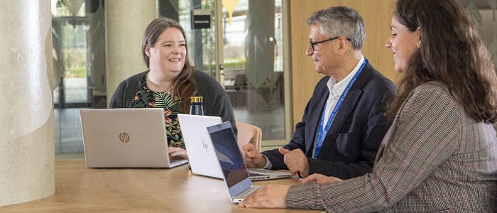 Three members of staff - two women and an older man - at a table in discussion with laptops. Source: Glasgow University photo library