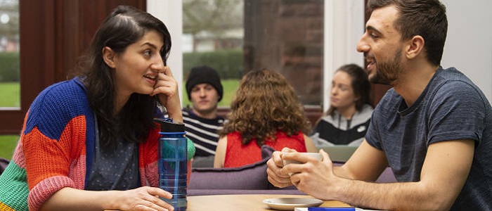 Two people, a woman and a man, sittting opposite each other at a table and having a chat: source: Glasgow University image library
