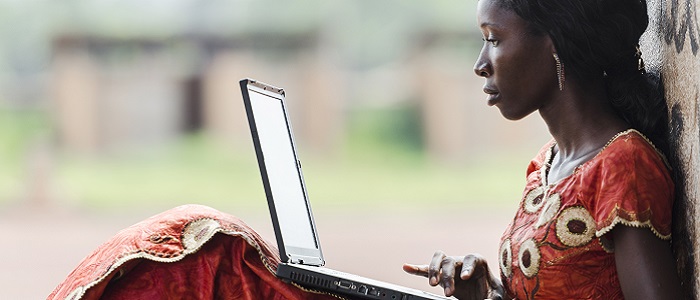 A black African woman in a red and yellow dress sitting with her back against a tree and looking at a laptop resting on her knees. Source: iStockPhoto https://www.istockphoto.com/photo/technology-symbol-african-woman-studying-learning-lesson-gm529835071-54284780