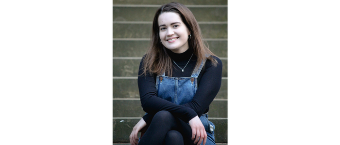 Young female wearing a black top and denim pinafore smiling at the camera