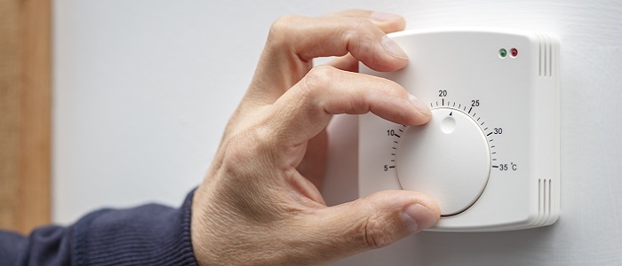 A man's hand adjusting a thermostat on a boiler. Source: BrianAJackson | IStockPhoto https://www.istockphoto.com/photo/central-heating-thermostat-control-adjustment-gm1348081831-425396053 