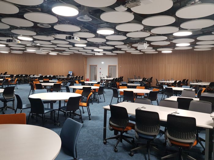 Flat floored teaching room with tables and chairs in groups.