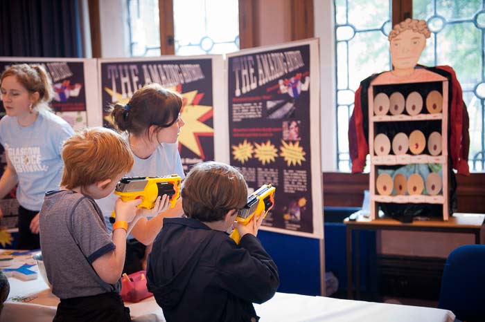 Photograph showing two GSF in Action students with two children. The children are holding toy shooters and are acting as antibodies. 